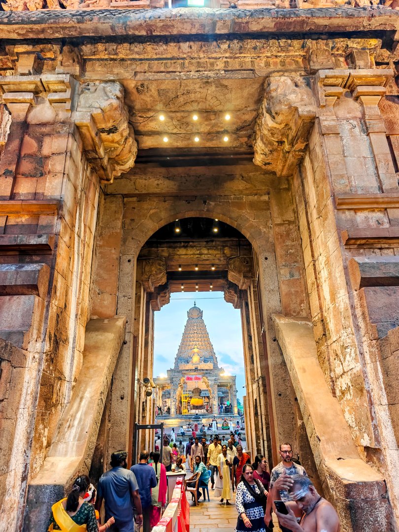 View through the entrance arch of Brihadisvara Temple, Thanjavur — worshippers and the main vimana tower visible in the distance